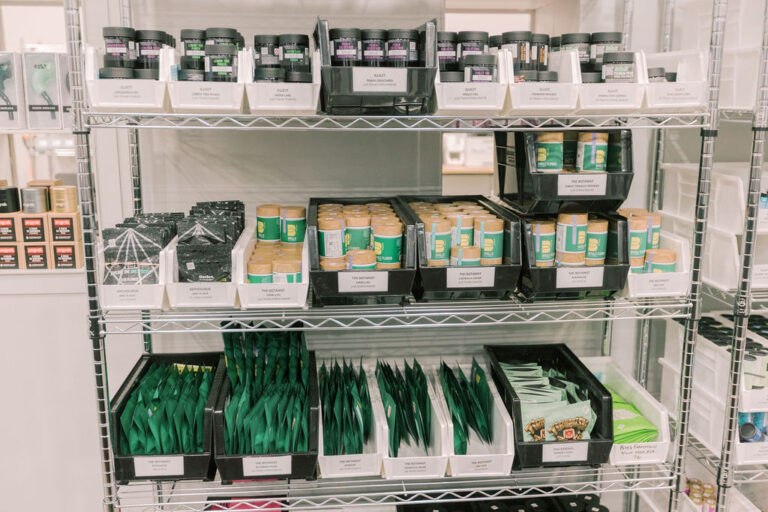 Metal shelves at La Vida Gardens dispensary stocked with cannabis products in green and black packaging.