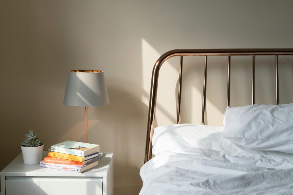 Sun coming through the window on a bed next to a nightstand stacked with books.
