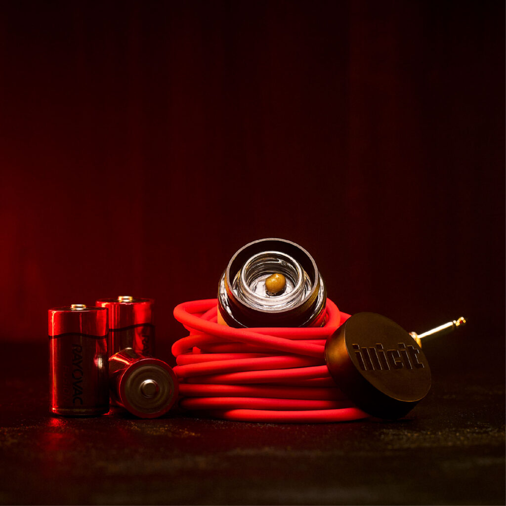 Open jar of cannabis live budder from brand ILLICIT sitting on top of an auxiliary cord.
