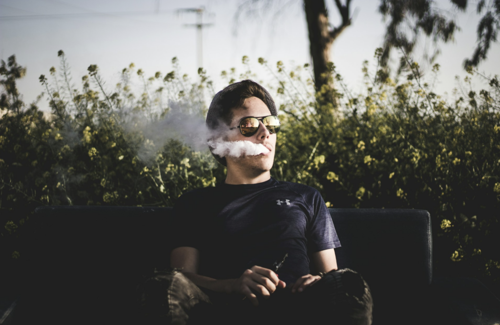 Person relaxing on a bench while exhaling vapor from a vape pen, illustrating the casual everyday use of cannabis vape cartridges in a legal market