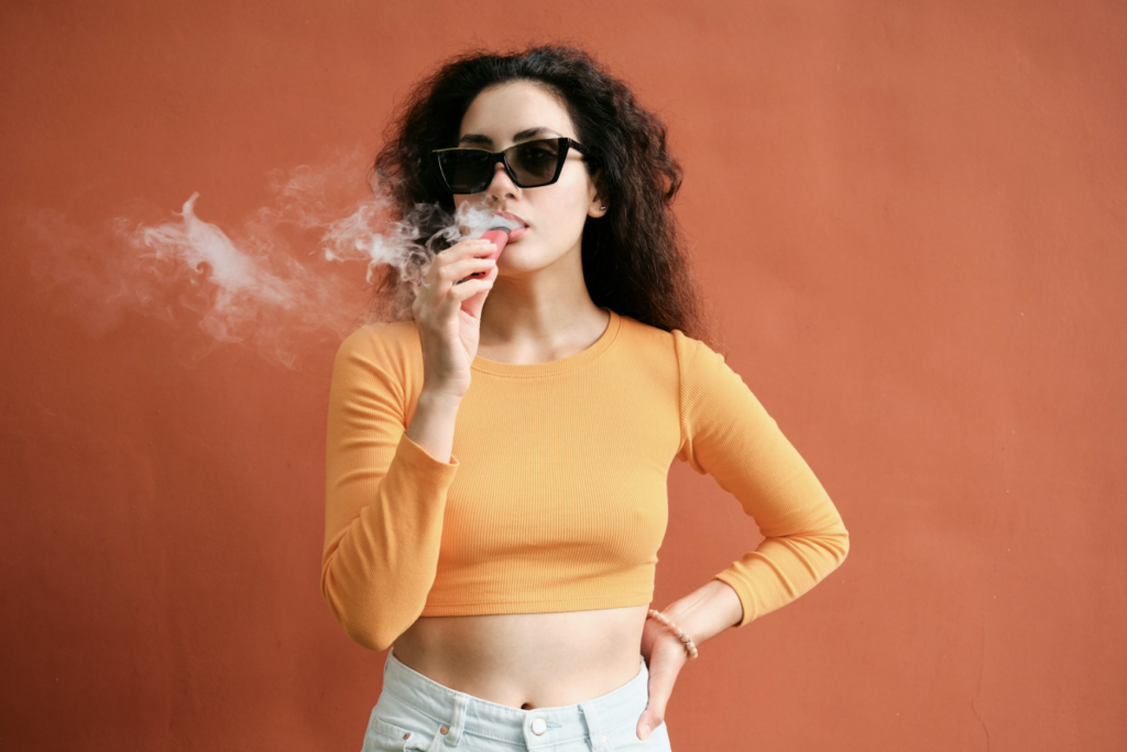 Woman exhaling vapor from a cannabis vape cartridge outdoors, demonstrating the kind of 510-thread vape pen used for live resin and distillate carts