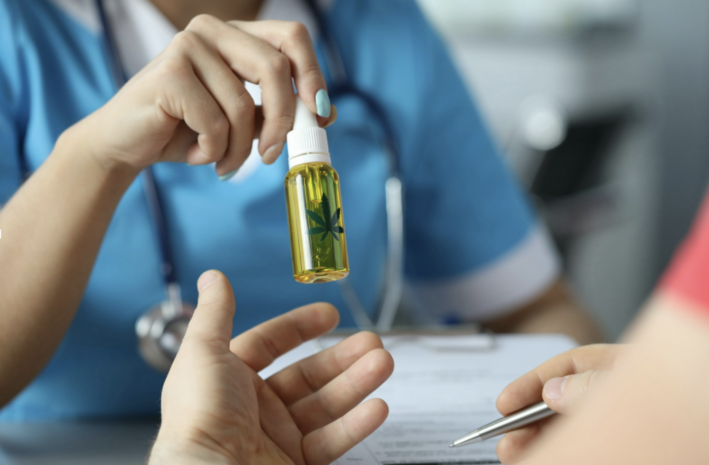 Source - Alt: Healthcare provider holding a cannabis oil tincture bottle during a consultation, representing the clinical dosing approach of starting THC at 2.5 mg and increasing gradually