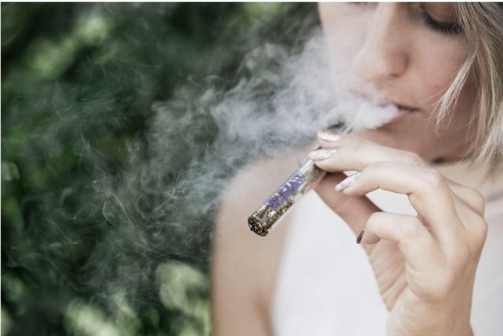Source - Alt: Close-up of a woman smoking a cannabis pre-roll outdoors, illustrating how 10 mg of THC feels different when smoked versus eaten as an edible due to liver metabolism