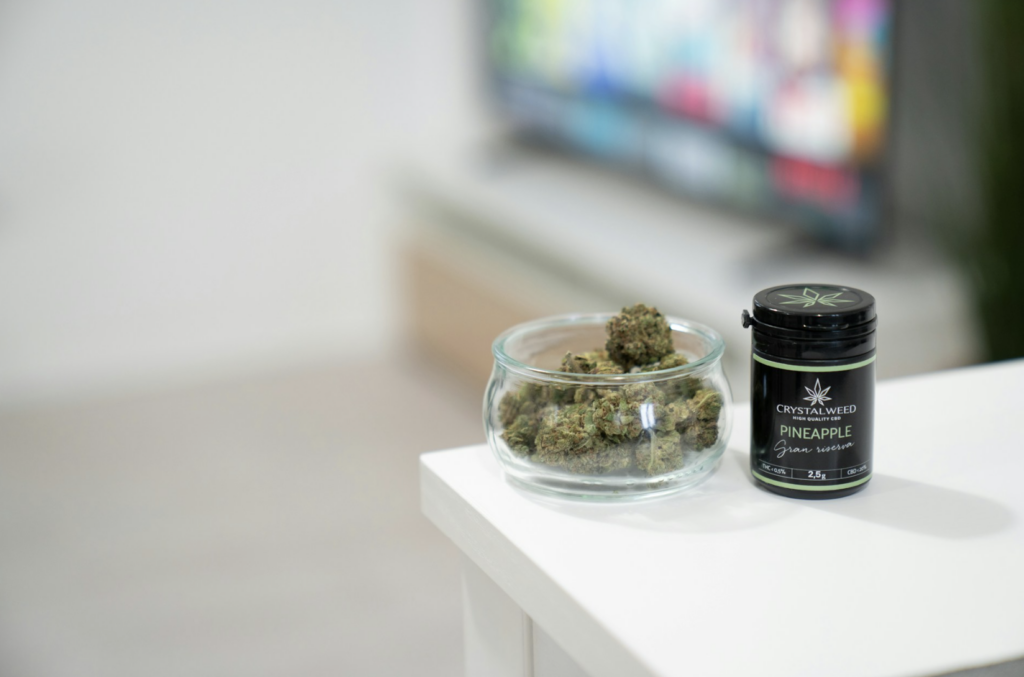 Cannabis flower buds in a glass jar next to a labeled dispensary container on a white shelf, representing the quarter-ounce purchase size that most regular NJ shoppers settle into
