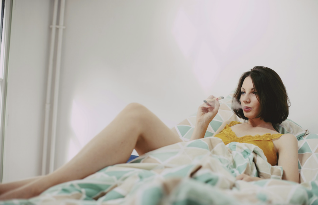 Woman smoking a cannabis joint while relaxing in bed before sleep, illustrating the recommended approach of one to two inhalations of a myrcene-heavy strain about an hour before bedtime