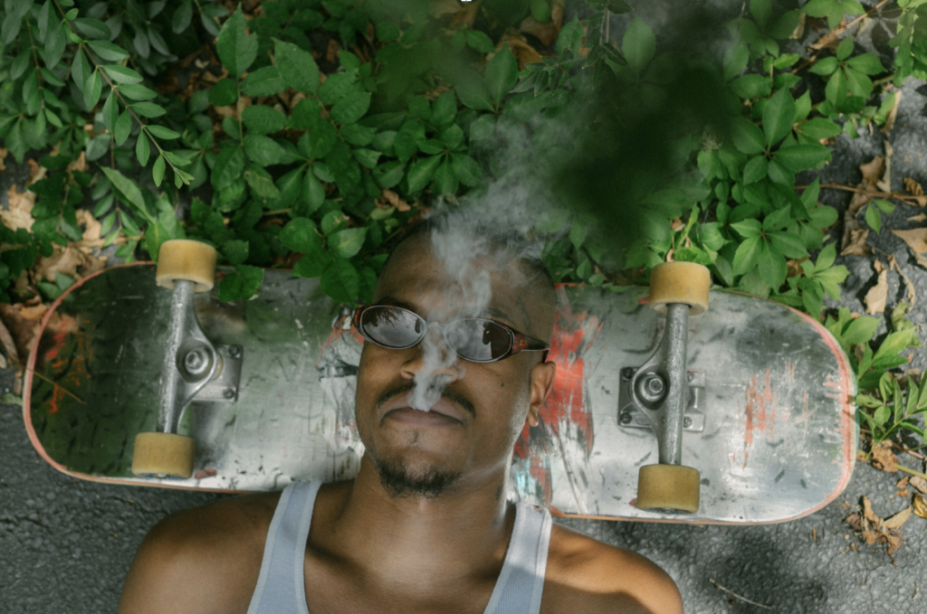 Person lying on the ground using a skateboard as a pillow while exhaling cannabis smoke, illustrating the couch-lock sedation produced by myrcene-rich strains like Granddaddy Purple